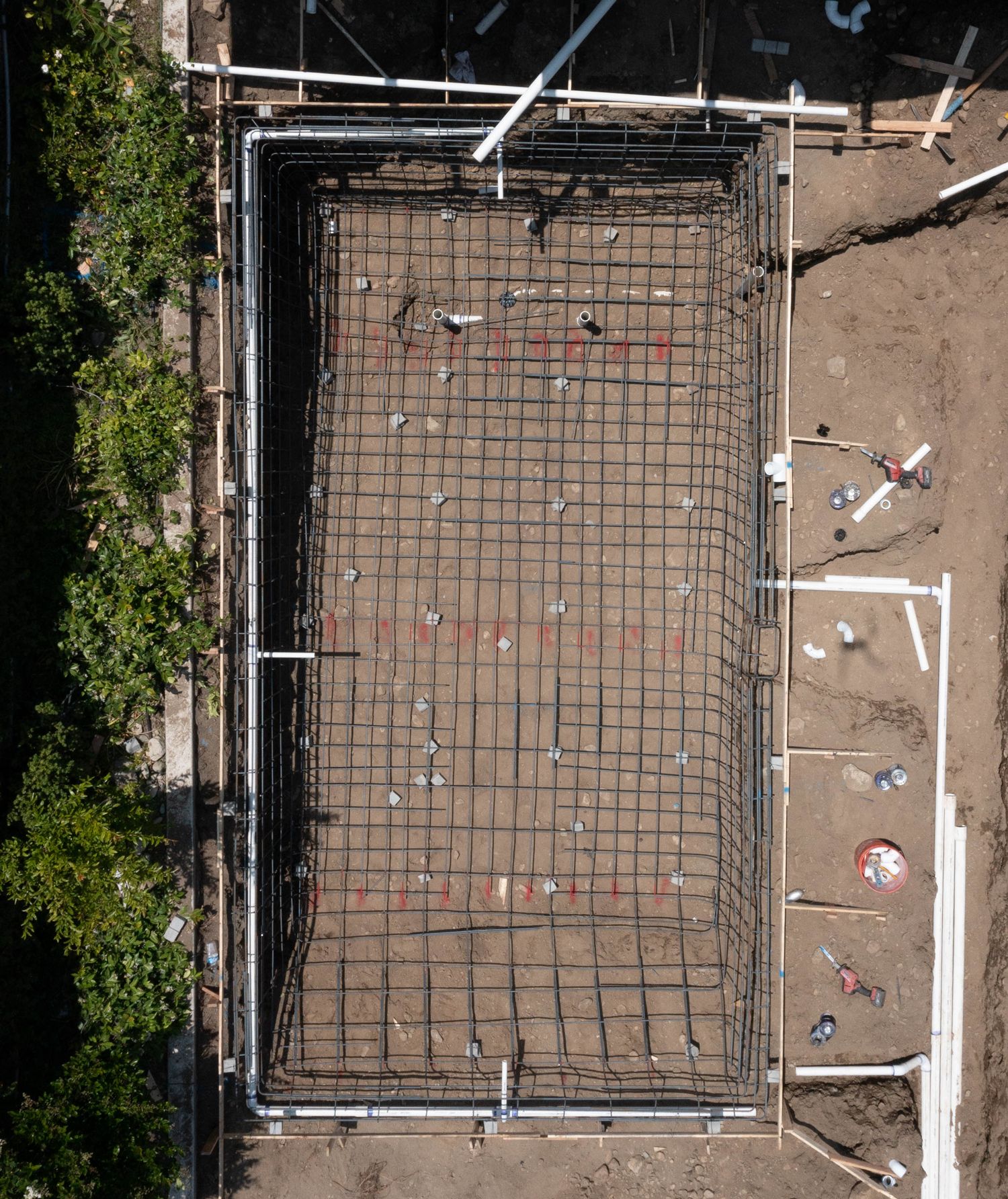 Aerial view of pool excavation showing steel rebar framework and plumbing pipes in place